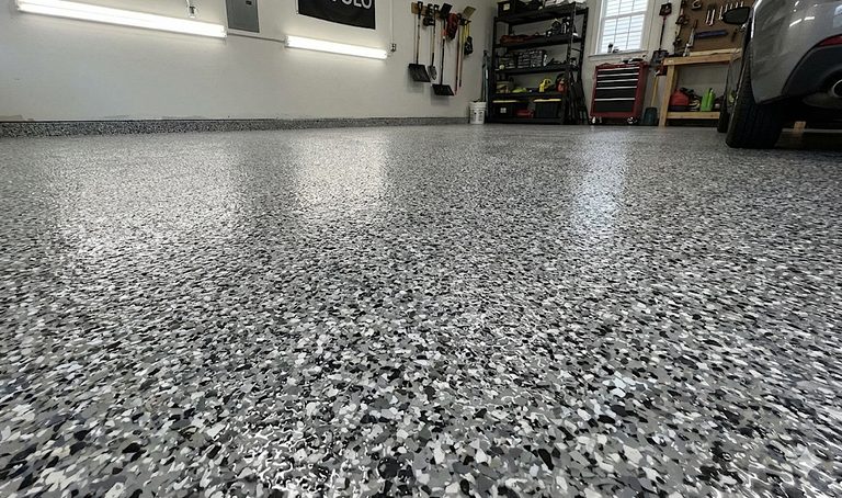 Speckled gray epoxy garage floor with shelves and a car in the background