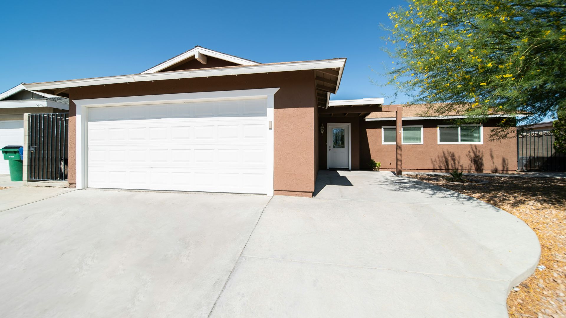 Concrete driveway with a smooth curved edge bordered by decorative rock landscaping in front of a single-story home