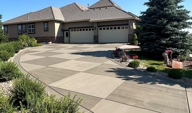 Curved concrete driveway leading to a beige house with a tiled roof and flowerbeds in front