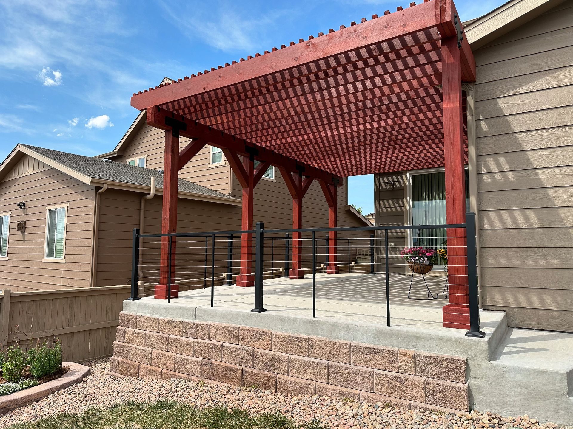 Covered backyard patio with red pergola roof, black railing, and concrete steps beside a house