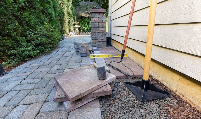 Outdoor paving stones and a house foundation under repair with a jack and support post