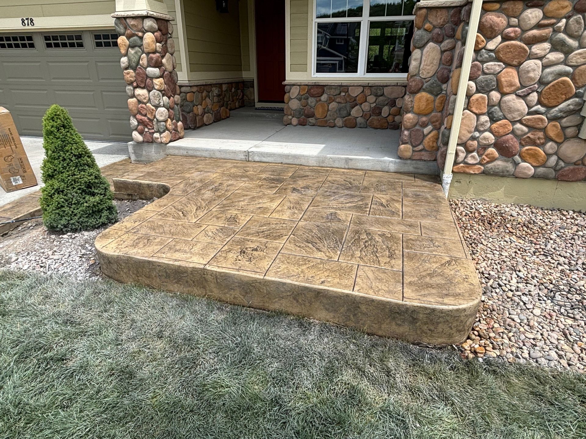 Front porch with stone facade and a small ramp leading to the entrance, bordered by gravel and a frosted lawn
