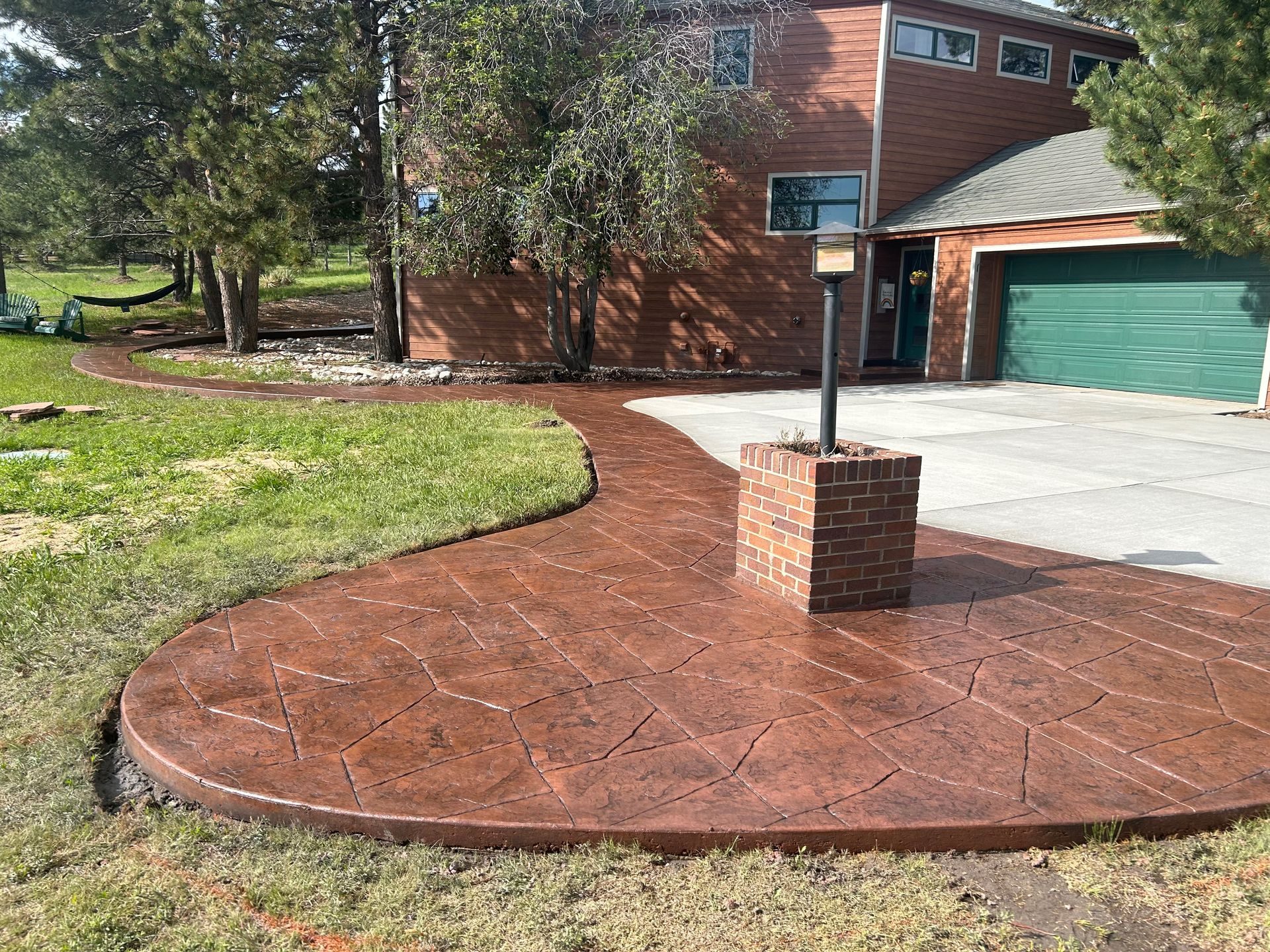 Curved red brick walkway leads to a driveway and green garage door beside a brick house and lawn