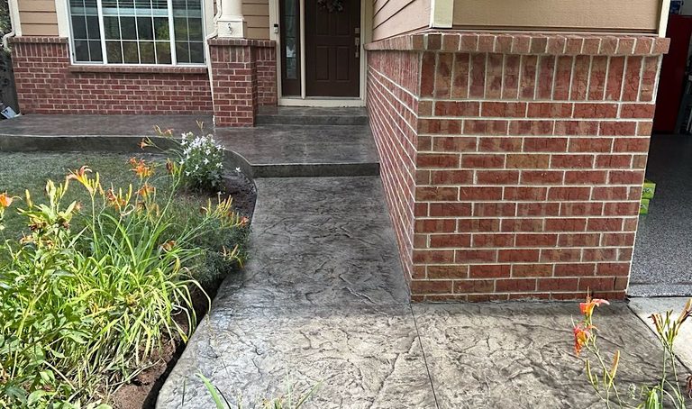 Concrete walkway leading to a brick building entrance beside a flower bed